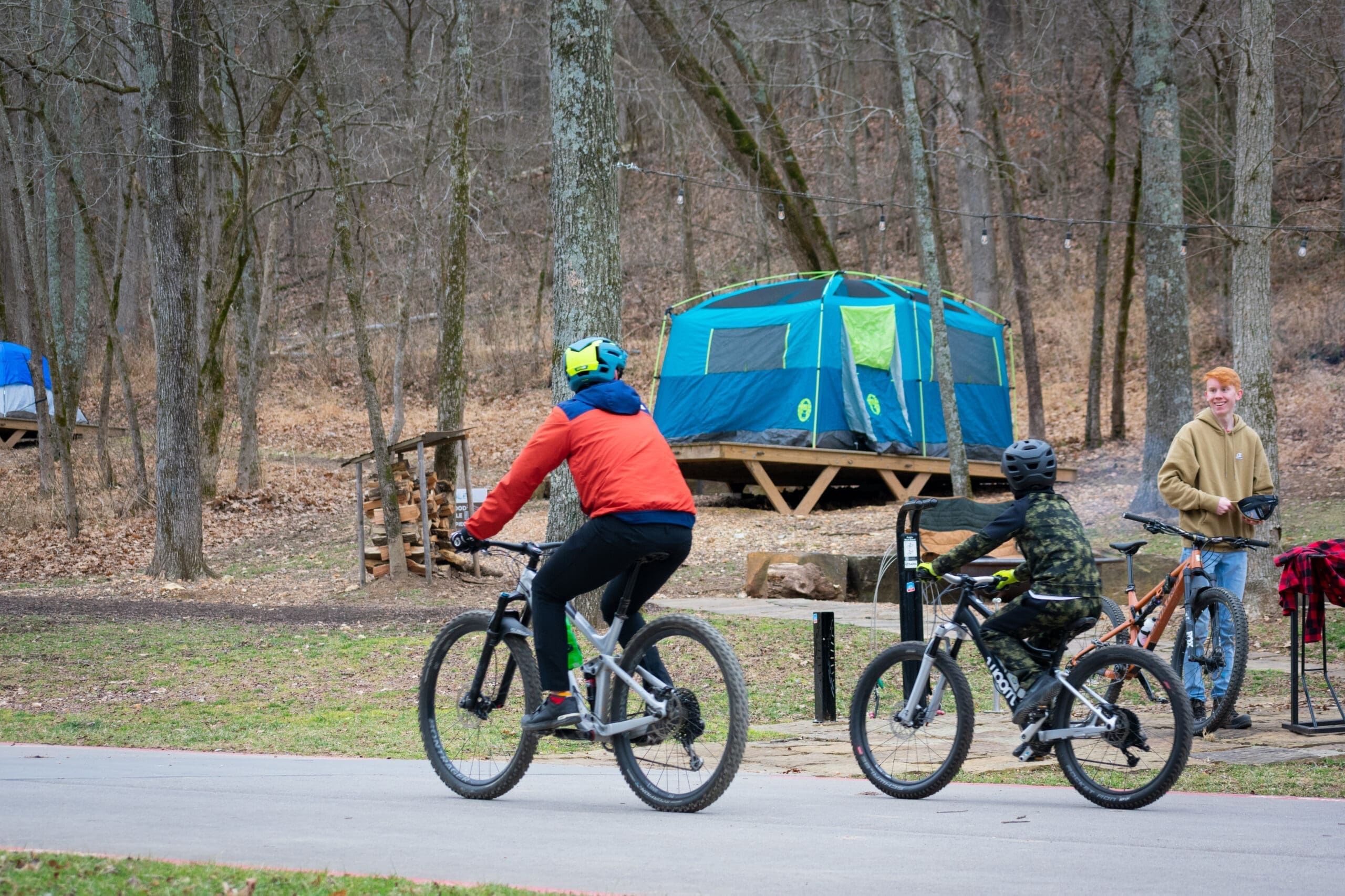 Family of four wearing helmets riding mountain bikes on paved trail through fall foliage, with vibrant autumn trees in background