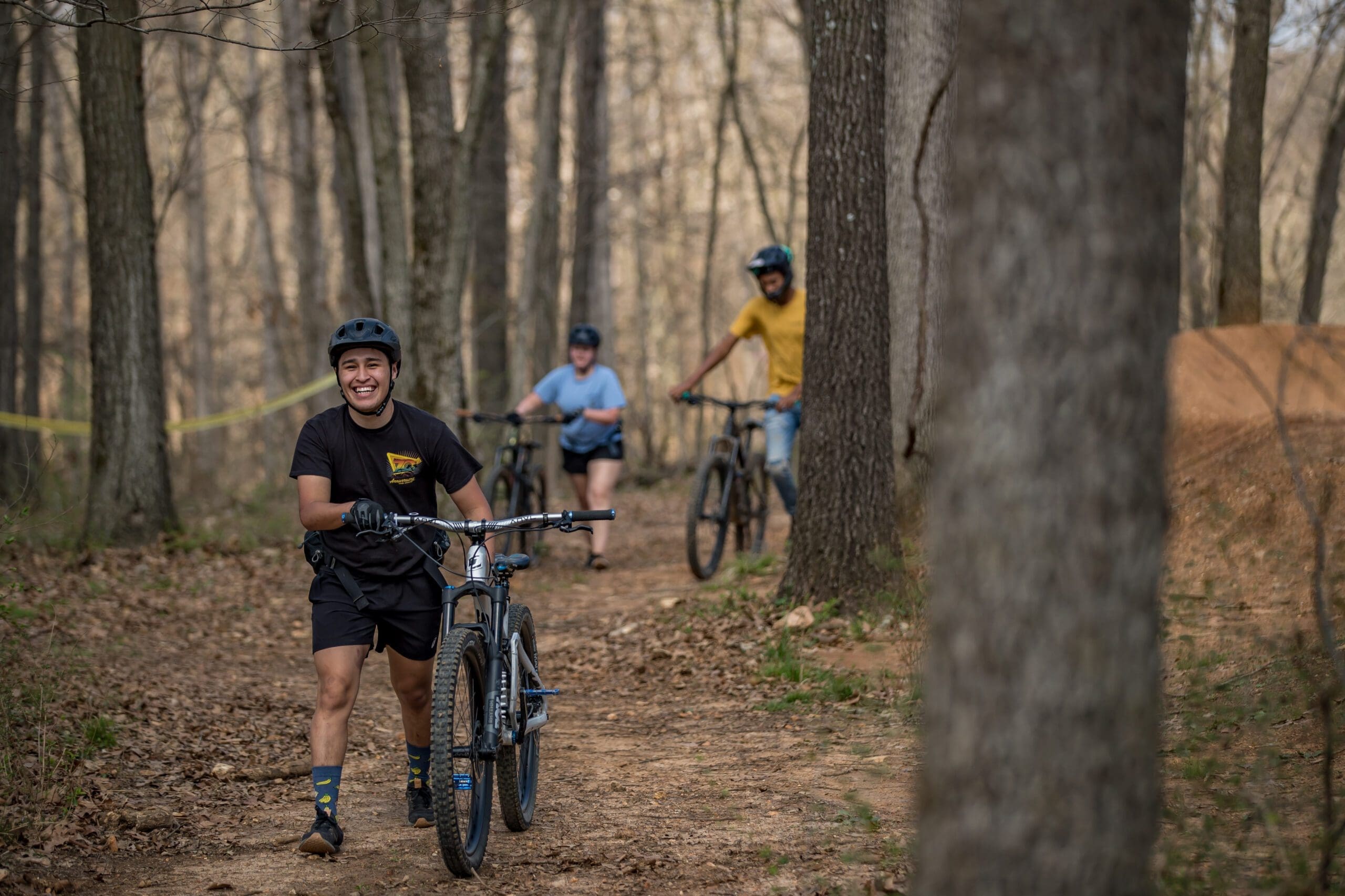 Family group of four mountain biking on natural dirt trail through dense autumn forest with golden and orange fall foliage