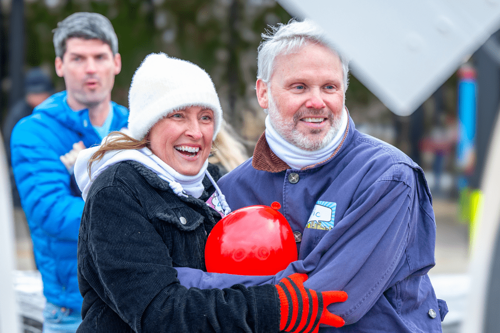 Smiling couple bundled up in winter clothing while playing archery games at The Quiver in Bentonville, AR, holding a red balloon.